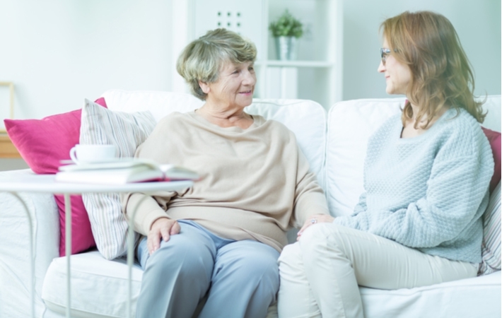 A middle-aged daughter conversing on the couch with her senior mother about the possibility of moving into a memory care community