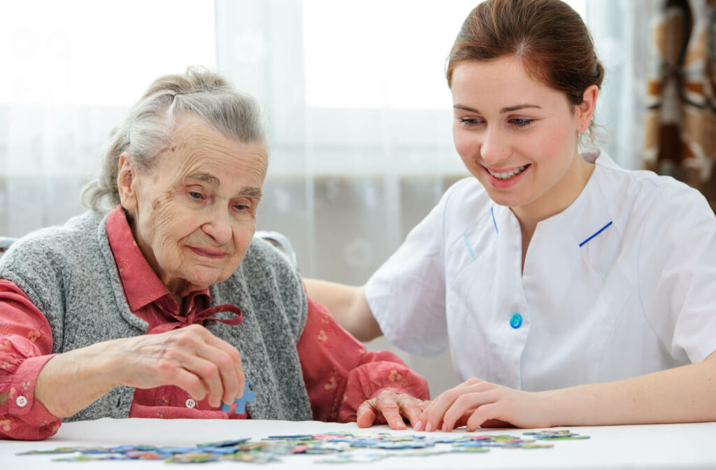 A female caregiver is playing a jigsaw puzzle with a senior woman in a memory care home.