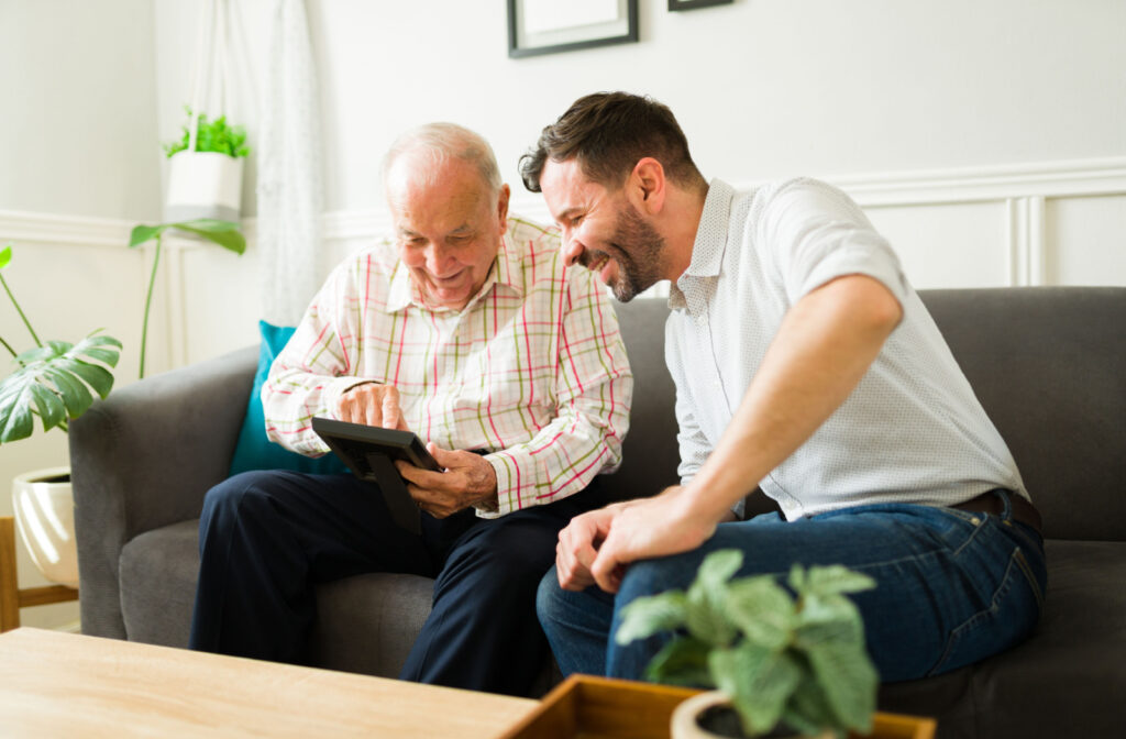 A senior and his son happily looking at a picture while sitting on a couch.